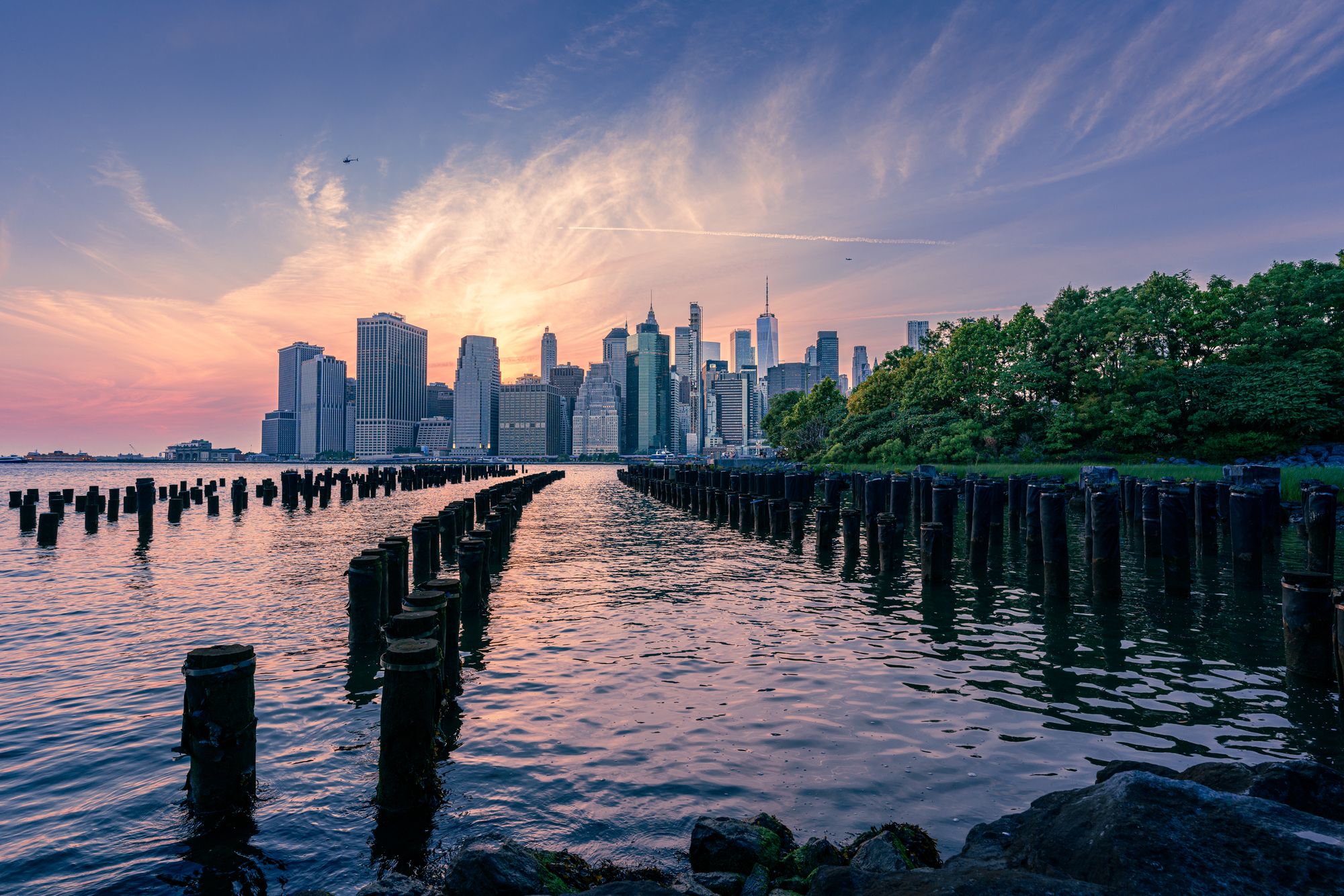 The Manhattan skyline across the waterfront under a dramatic pastel sunset